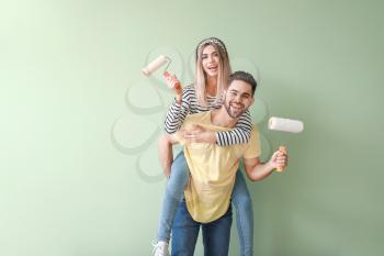 Young couple with paint rollers near color wall in new apartment�