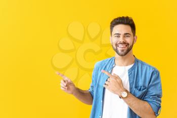 Handsome young man pointing at something on color background�