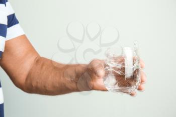 Senior man with Parkinson syndrome holding glass of water on grey background�