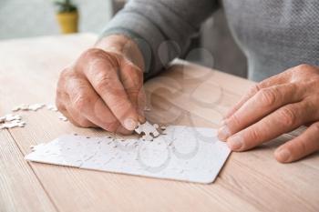 Senior man with Parkinson syndrome doing puzzle at home, closeup�