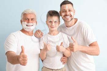Man, his father and son with shaving foam on their faces showing thumb-up gesture on color background�