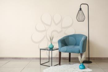 Comfortable armchair, table and lamp near color wall�
