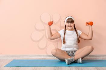 Overweight girl doing exercises near color wall�