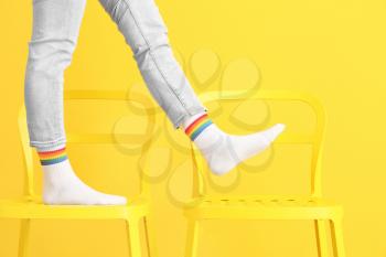 Legs of young woman in socks standing on chairs against color background�