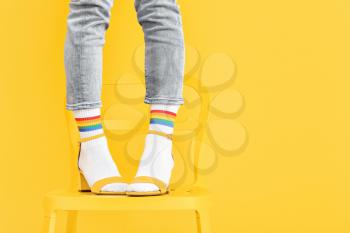 Legs of young woman in socks and sandals standing on chair against color background�