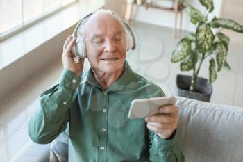 Elderly man with mobile phone and headphones at home�