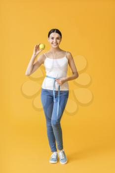 Young woman with measuring tape and apple on color background. Weight loss concept�
