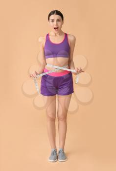 Shocked young woman with measuring tape on color background. Weight loss concept�