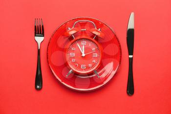 Plate and cutlery with alarm clock on color background�