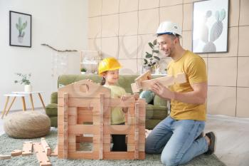 Father and little daughter dressed as builders playing with take-apart house at home�