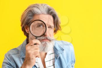 Funny elderly man with magnifier on color background�