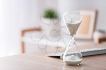 Hourglass with computer keyboard on table in office. Time management concept�