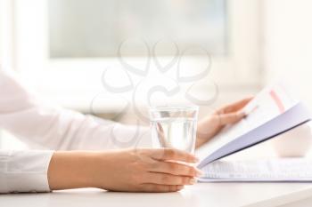Woman drinking water while reading newspaper at table�