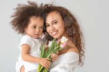 Little African-American girl with her mother and bouquet on light background�