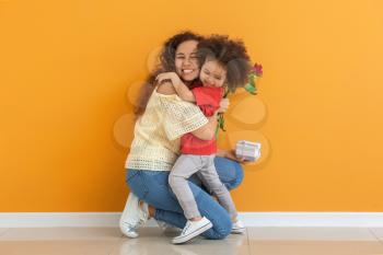 Little African-American girl greeting her mother near color wall�
