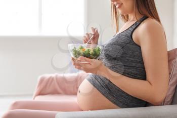 Beautiful pregnant woman eating healthy salad at home�