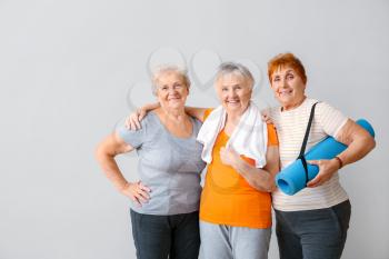 Happy elderly women with yoga mat on light background�