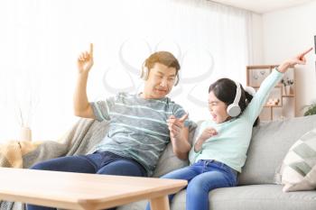 Happy Asian man and his little daughter listening to music at home�