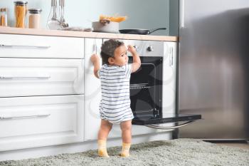 Little African-American baby near stove in kitchen. Child in danger�