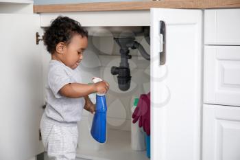 Little African-American baby playing with detergents at home. Child in danger�