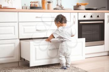 Little African-American baby playing in kitchen. Child in danger�