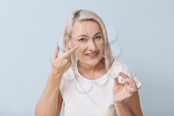 Mature woman putting in contact lenses against light background�
