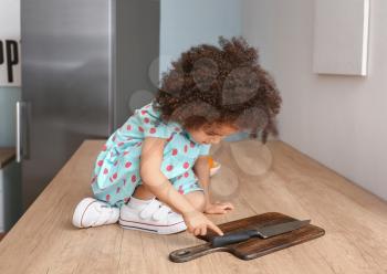 Little African-American girl playing with knife in kitchen. Child in danger�