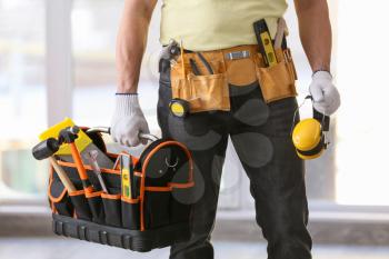 Male builder holding bag with tools and headphones in office�
