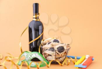 Tasty hamantaschen, gragger and party decor for Purim holiday and bottle of wine on color background�