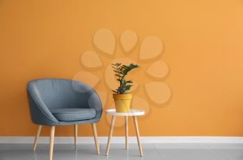 Comfortable armchair and table with houseplant near color wall�