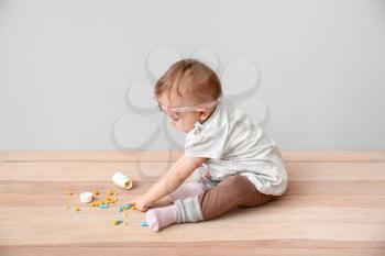 Little baby with medicines on grey background. Child in danger�