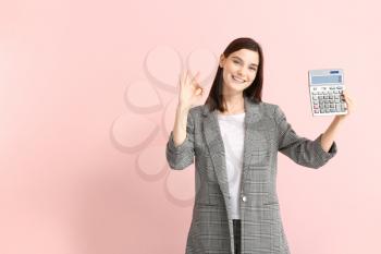Young woman with calculator showing OK on color background�