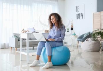Woman sitting on fitness ball while working at home�