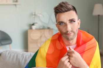Portrait of young transgender woman with flag of LGBT at home�