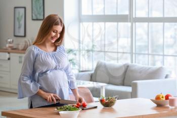 Beautiful young pregnant woman cooking in kitchen�