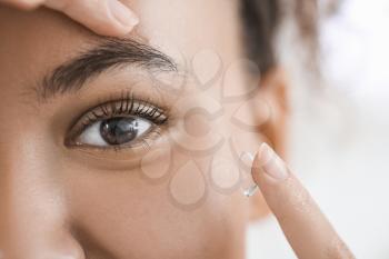 Young African-American woman putting in contact lenses, closeup�