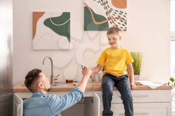 Little son helping his father to repair sink in kitchen�