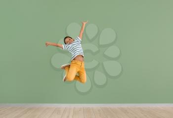 Little African-American boy jumping against color wall�