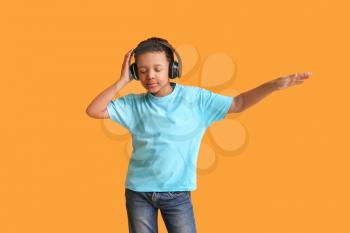 Little African-American boy listening to music and dancing against color background�