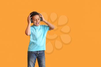 Little African-American boy listening to music against color background�