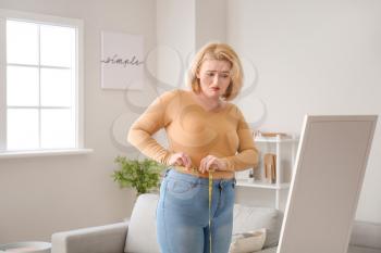 Sad overweight woman with measuring tape at home. Weight loss concept�