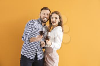 Happy couple with glasses of wine on color background�