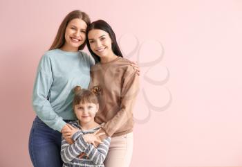 Happy lesbian couple with little adopted girl on color background�