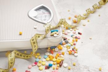 Weight loss pills, scales and measuring tape on grey background�