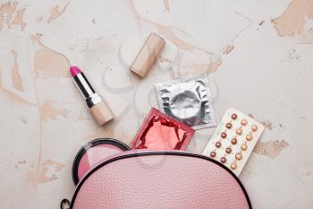 Female bag with contraceptive pills, condoms and cosmetics on white background�