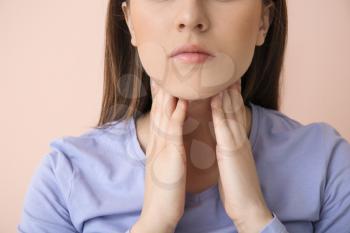 Young woman checking thyroid gland on color background, closeup�