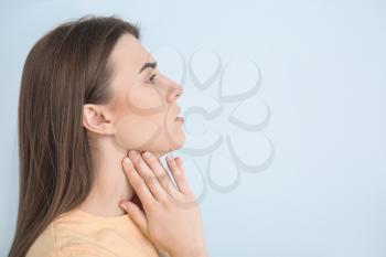 Young woman checking thyroid gland on color background�
