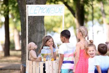 Adorable children waiting in queue for natural lemonade near stand in park�