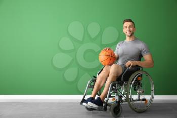 Young basketball player sitting in wheelchair against color wall�