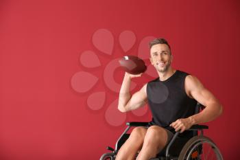 Young man with rugby ball sitting in wheelchair on color background�